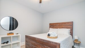 Un dormitorio con cama de madera, espejo redondo, consola blanca y mesita de noche con lámpara.
