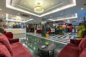 Un'ampia hall con una reception, posti a sedere rossi, una scala e un lampadario.