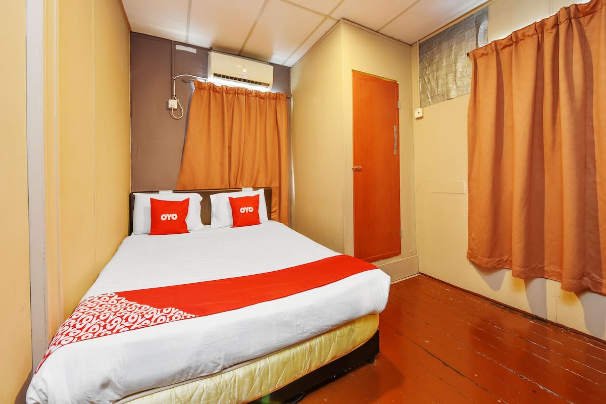 A hotel room with a bed, orange curtains, a wooden door, and an air conditioning unit on the wall.