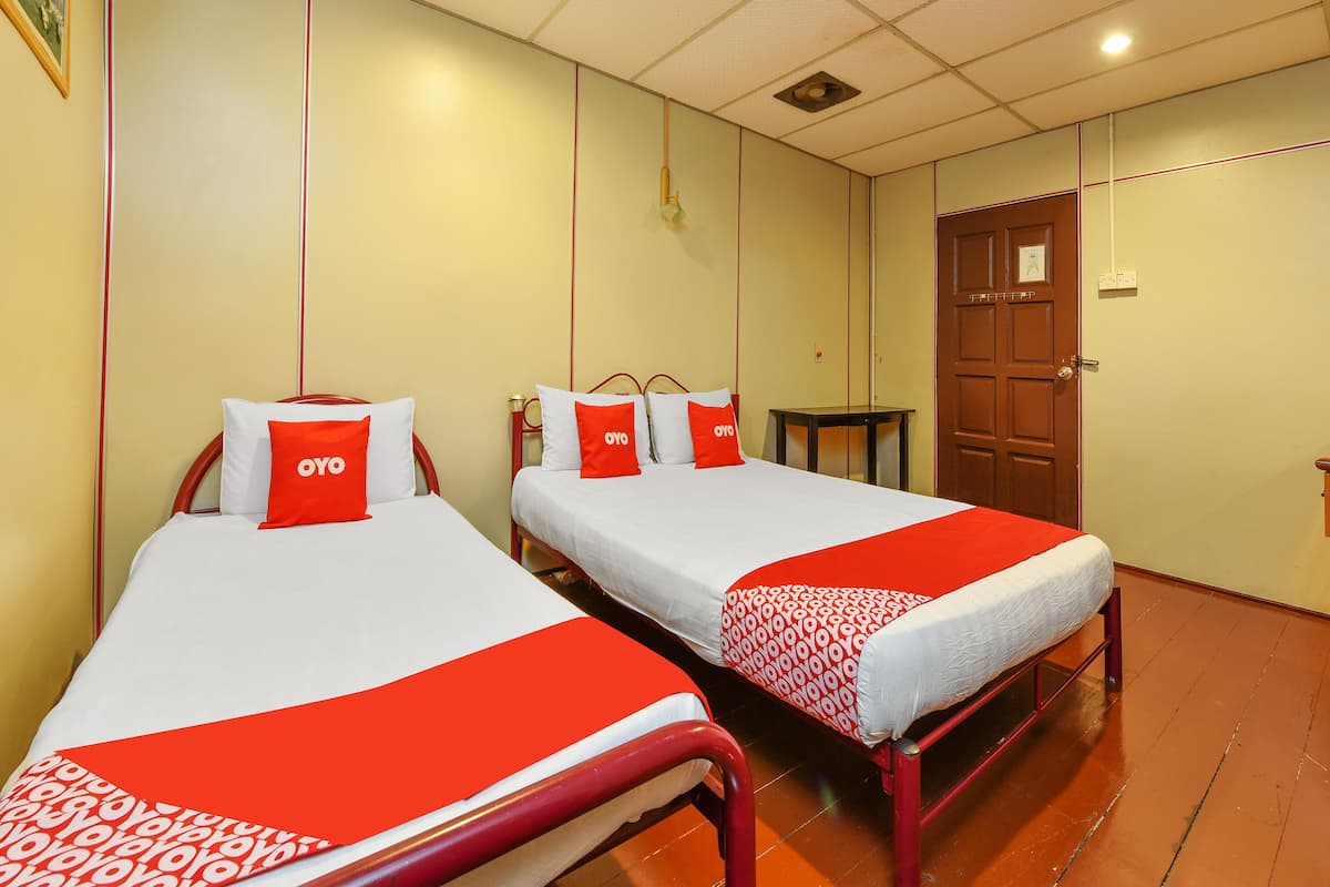 A hotel room with two beds, each with red and white bedding, a small table, and a wooden door.