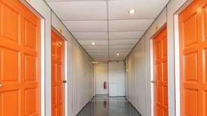 A hallway with orange doors on both sides, a fire extinguisher mounted on the wall, and a ceiling with recessed lighting. - Hotel O Pulau Ketam Inn (Pulau Ketam)