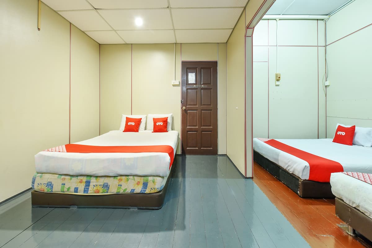 A hotel room with two beds, each with red pillows and a floral bedspread. The room has a wooden floor and beige walls.