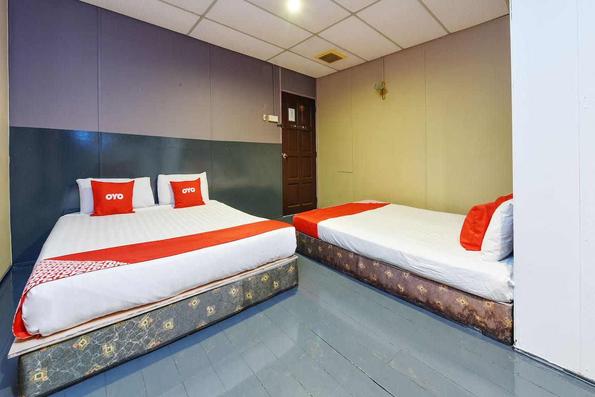 A hotel room with two beds, each with white bedding and red accents, a patterned floor, and a ceiling with recessed lighting.