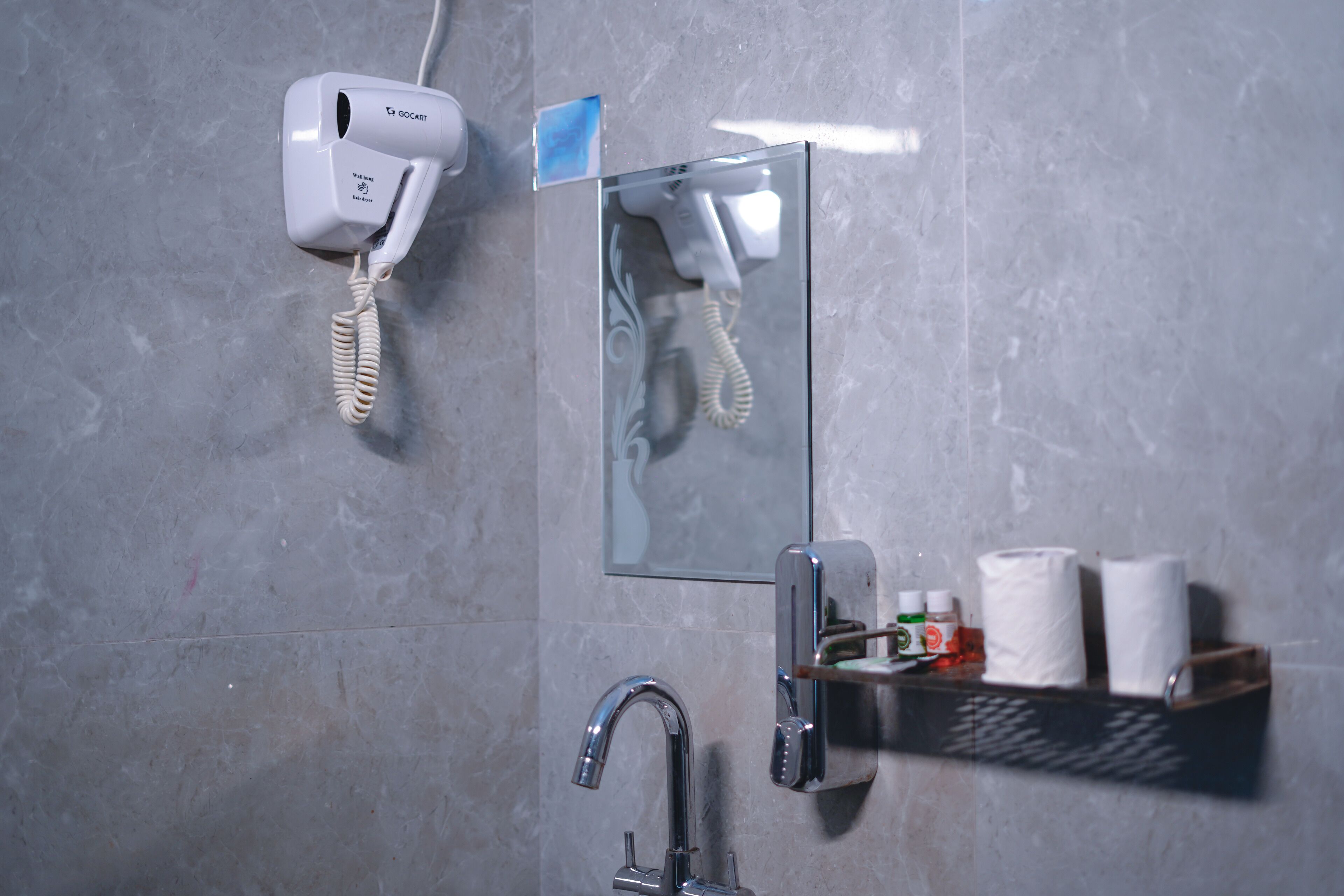 Et badeværelse med en hårtørrer, et spejl, en vask og en hylde med toiletartikler.