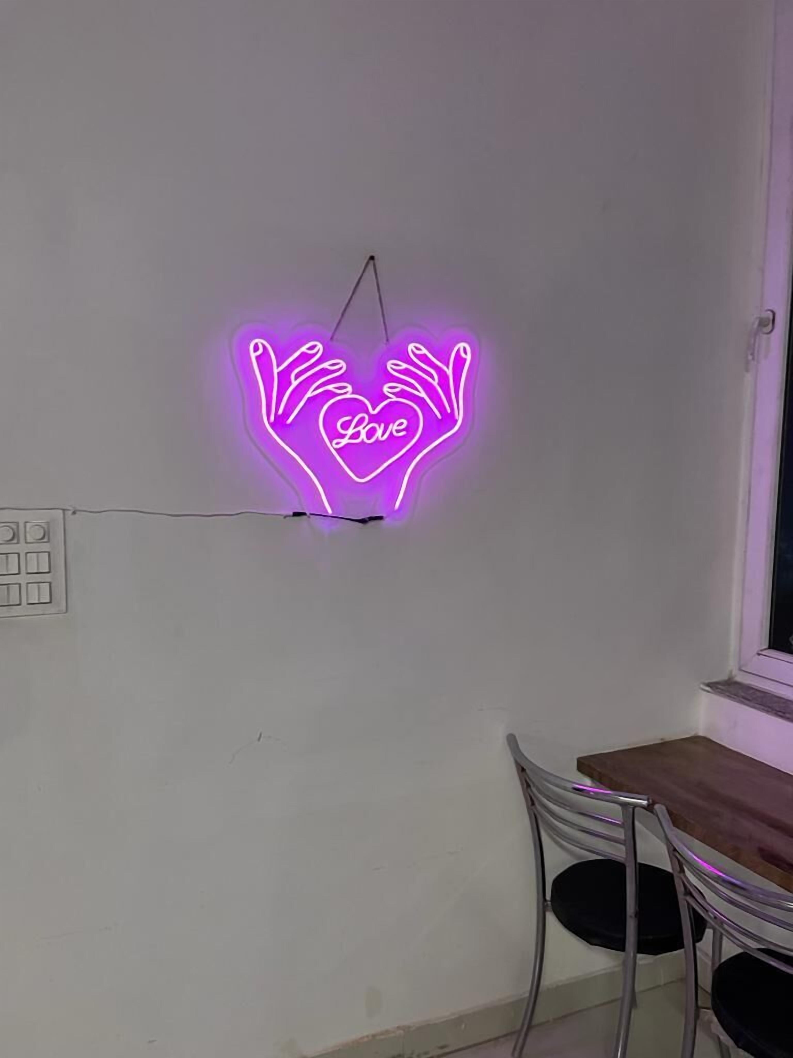 A neon sign with a heart and the word "Love" in a room with a window and a table with chairs.