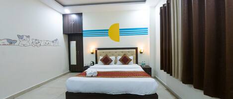 Habitación de hotel con cama, mesita de noche, espejo, pared decorada con un gato y ventana con cortinas.