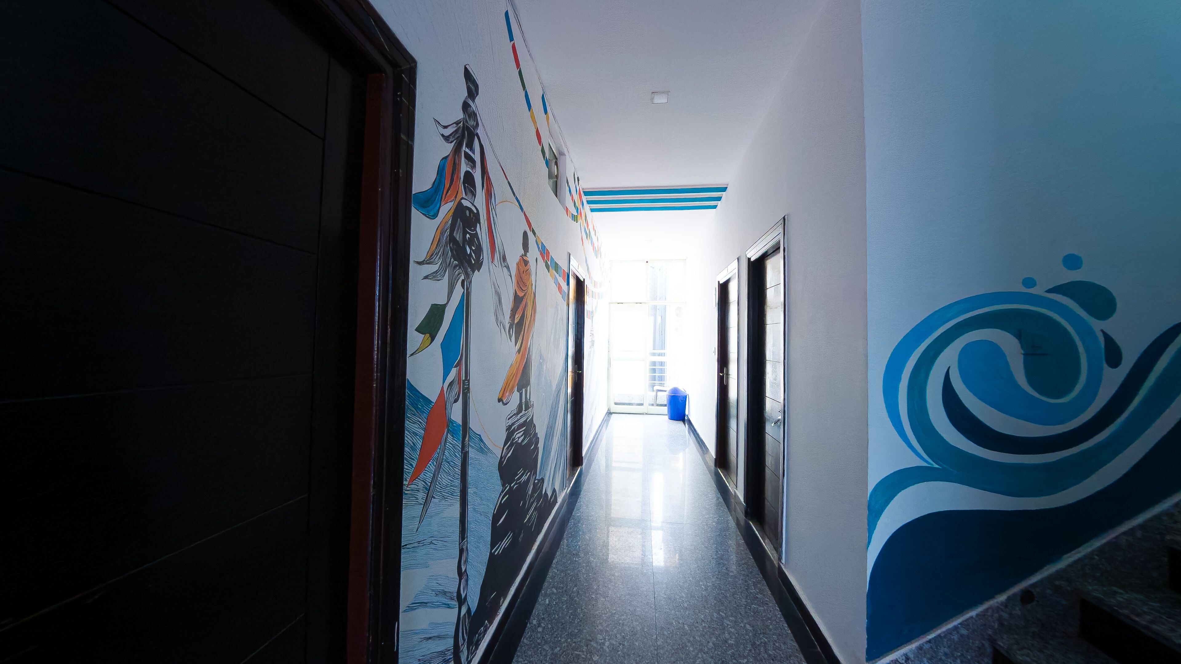 A hallway with a long corridor, a door on the left, and a blue wall with a wave design on the right.
