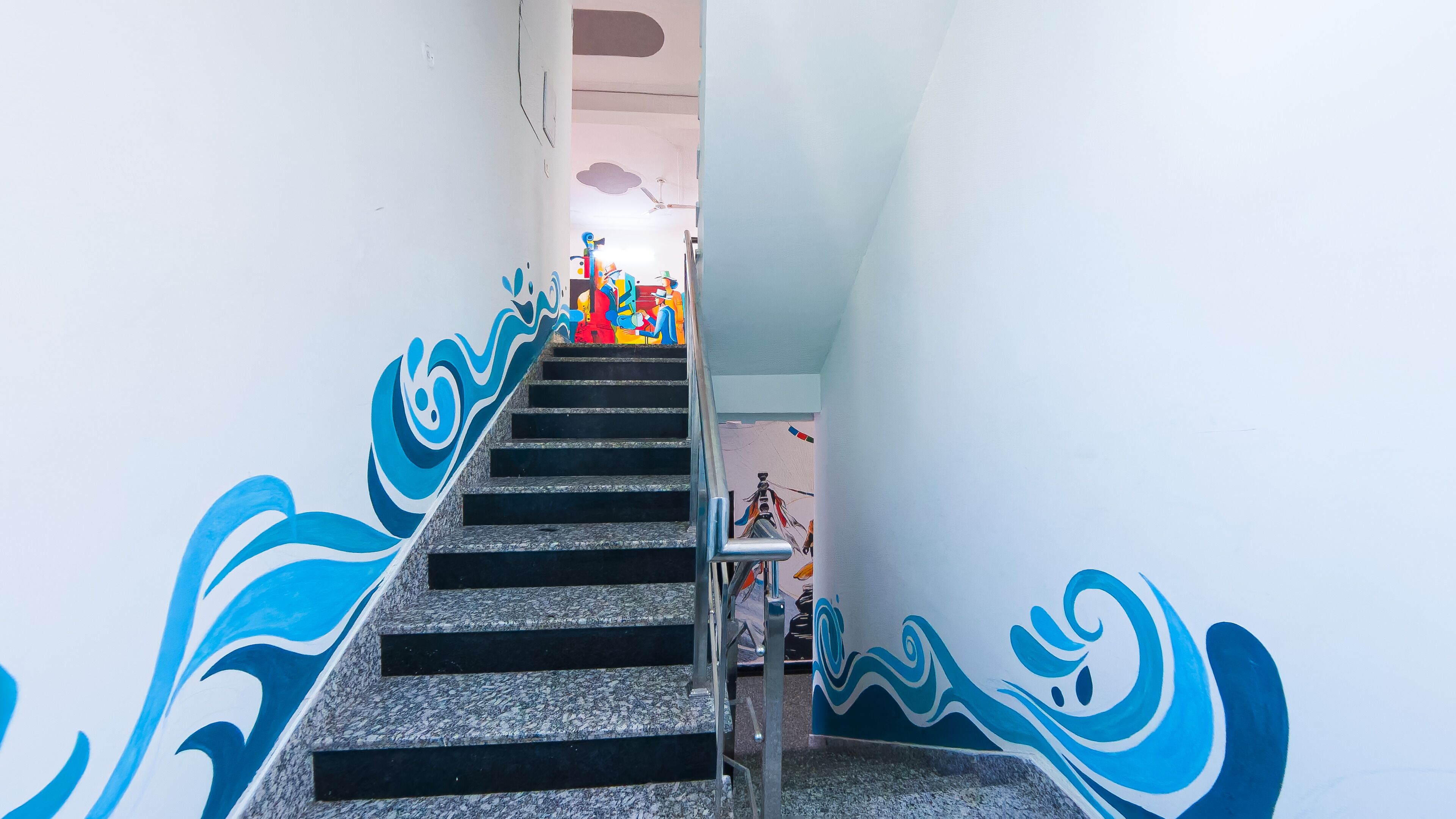A staircase with blue wave patterns on the walls, leading to a room with a bed and a ceiling fan.