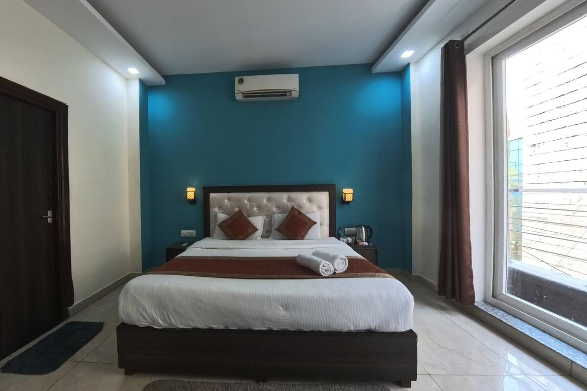 A bedroom with a large bed, a dark wooden door, a blue accent wall, and a window with curtains.