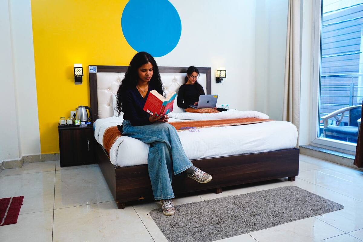 A bedroom with a bed, a nightstand, a lamp, and a window with a view.