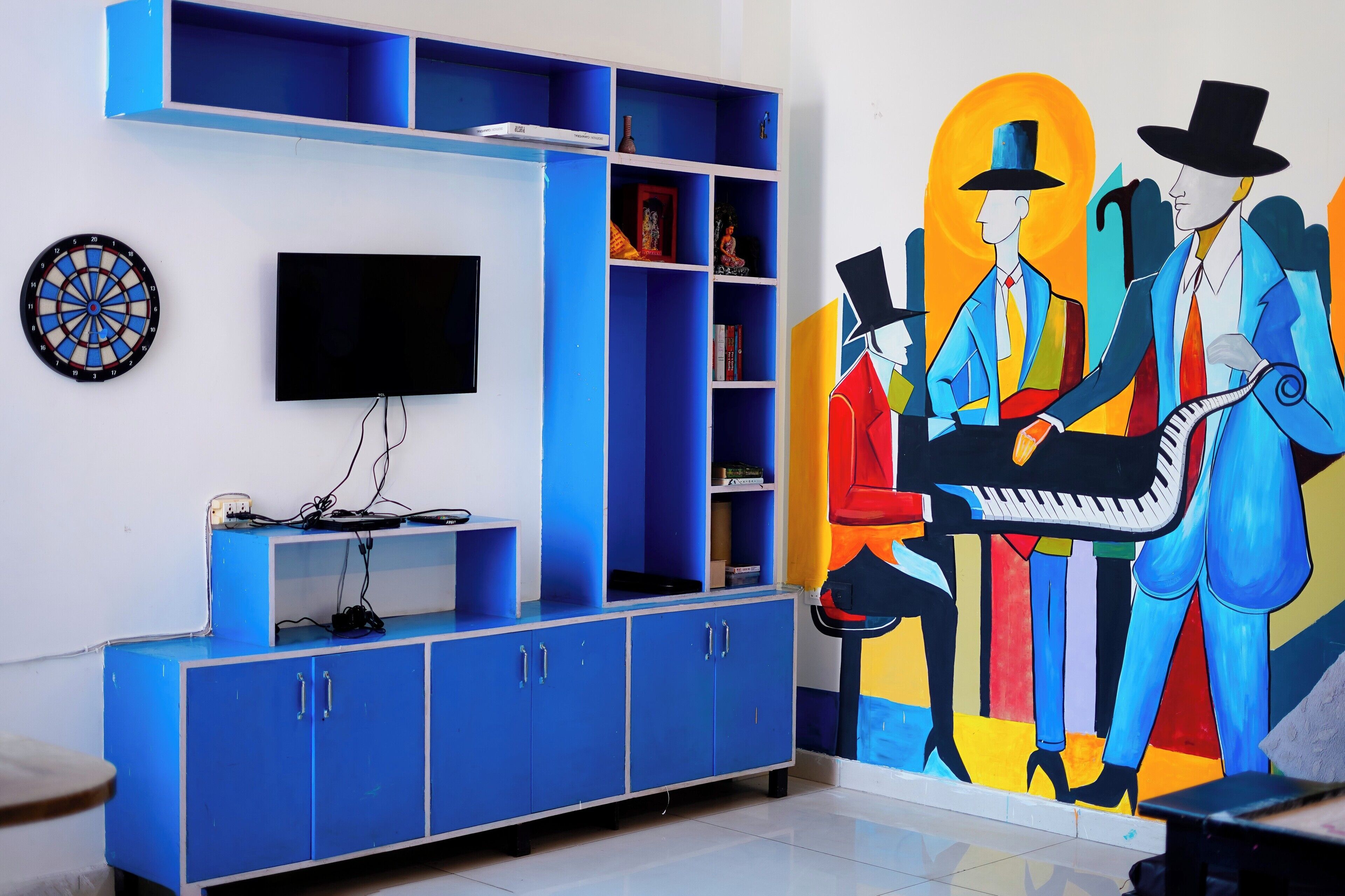 A room with a blue entertainment unit, a flat-screen TV, a dartboard, and a colorful abstract painting on the wall.