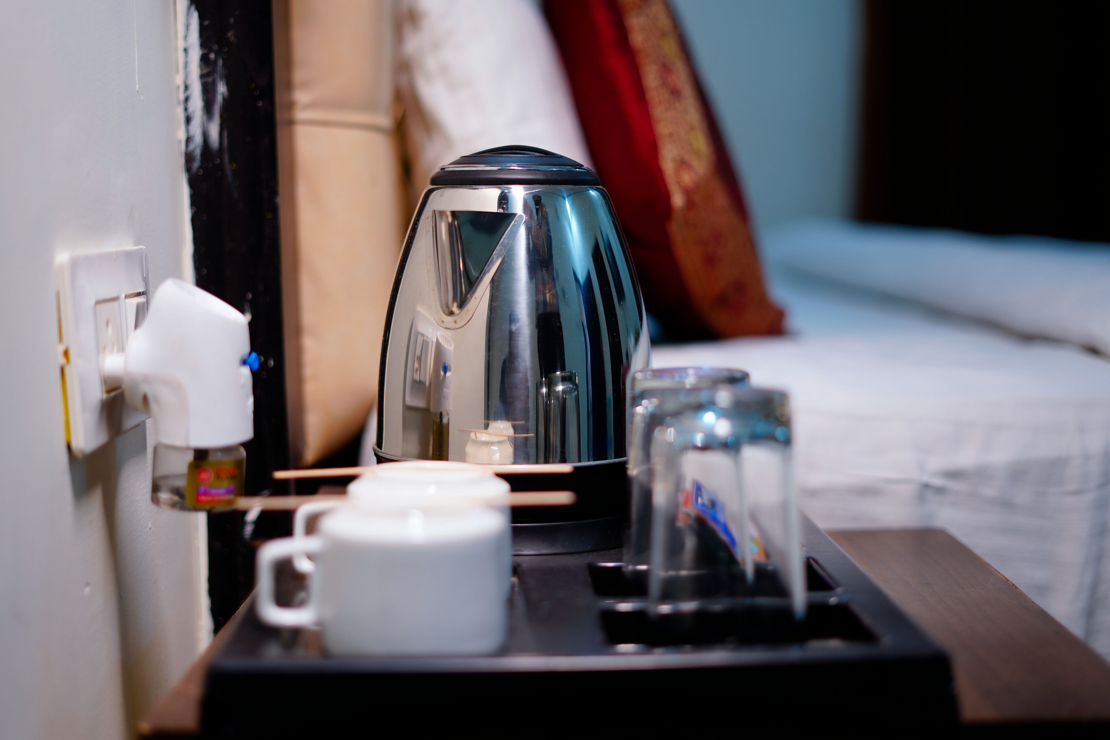 A hotel room with a bedside table featuring a coffee maker, a glass, and a white mug.