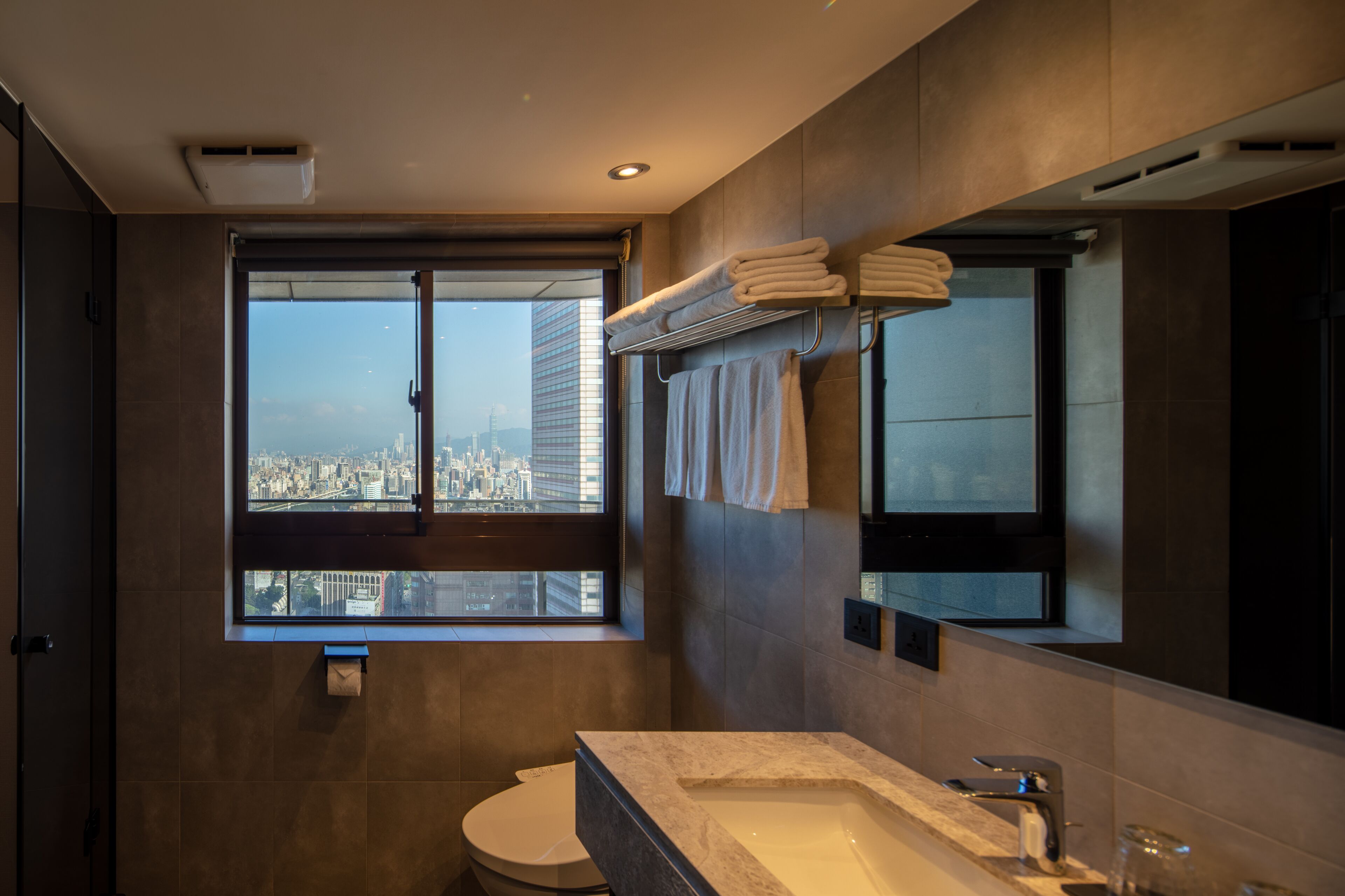 A modern bathroom with a large window, a bathtub, and a toilet.