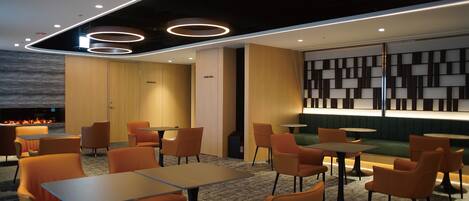 A modern restaurant with orange chairs and tables, a fireplace, and a wall with geometric patterns.