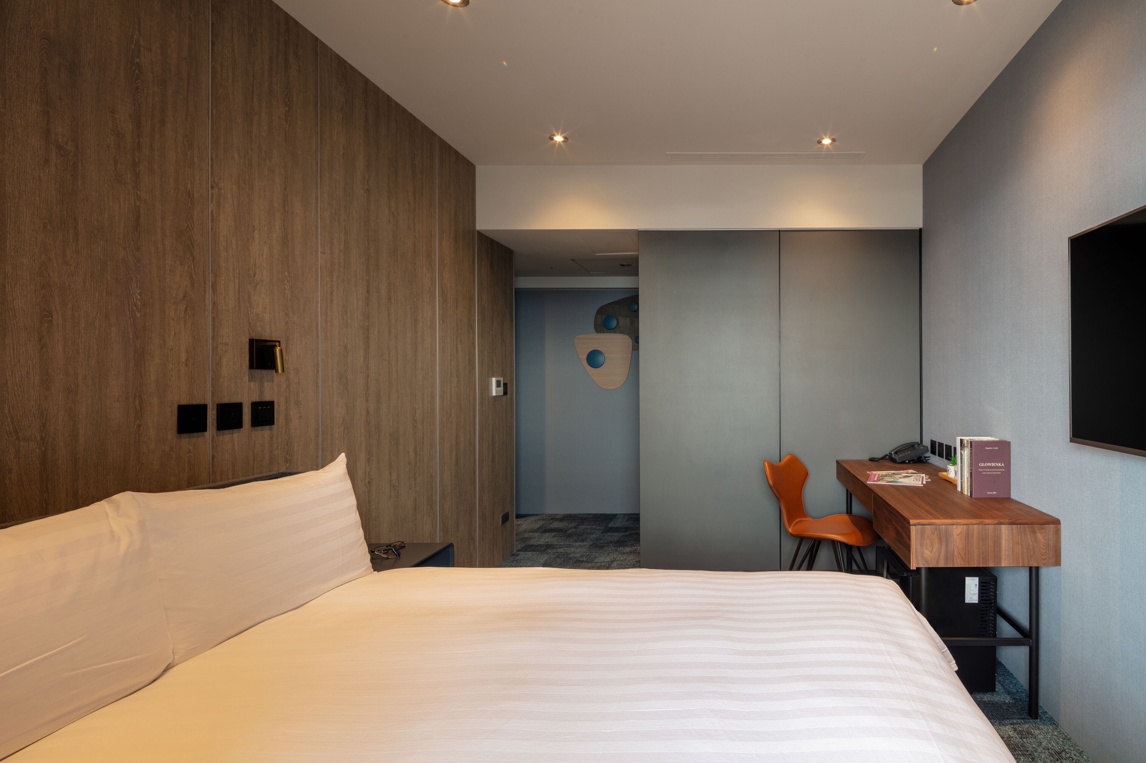 A modern hotel room with a large bed, a desk with a chair, and a TV mounted on the wall.