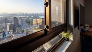A modern room with a large window overlooking a cityscape, a potted plant, and a flat-screen TV mounted on the wall. - Roaders Plus Hotel Taipei Station (Taipei)