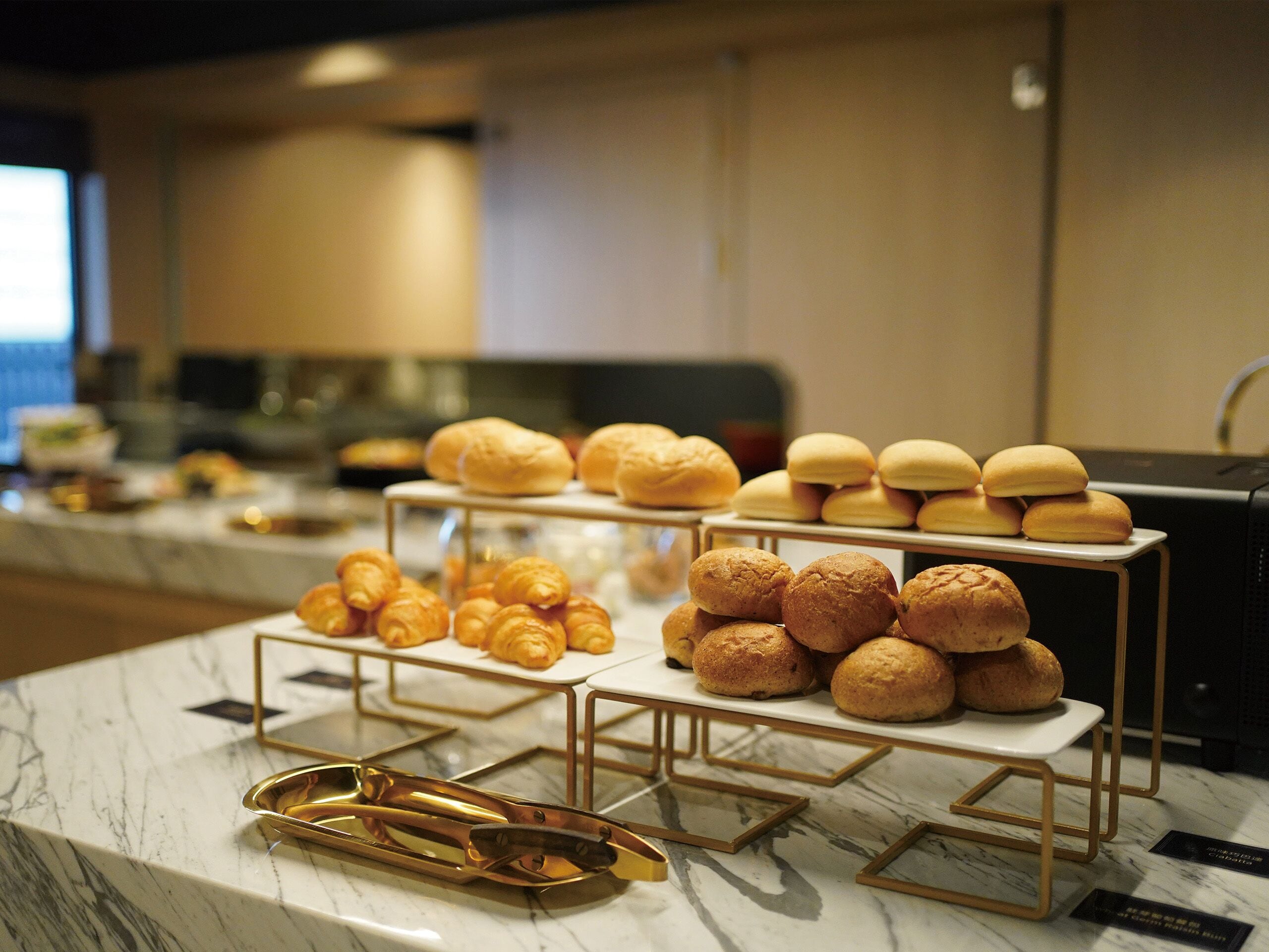 Buffet com diversos pães e doces dispostos em suportes escalonados.
