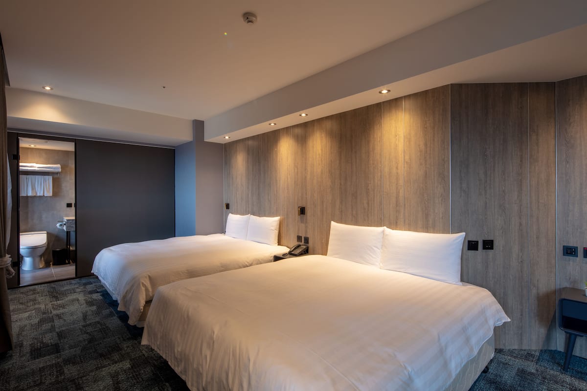 A hotel room with two beds, a bathroom, and a mirror.