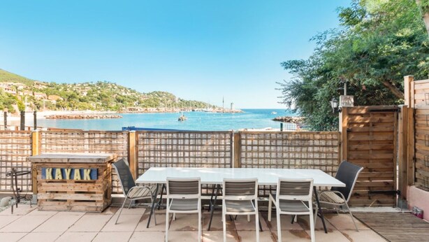 Eine Terrasse mit Tisch und Stühlen, ein Holzschild mit der Aufschrift KAYAK und Blick auf das Meer sowie eine in der Ferne liegende Stadt.