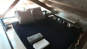 Ein Bett mit dunkelblauer Matratze, zwei Kissen und einem kleinen Nachttisch mit einer Lampe.