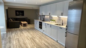 A modern kitchen with white cabinets, a stainless steel refrigerator, and a dining area with a sofa and coffee table. - Notodden Sentrum Apartment NO 9 (Notodden)