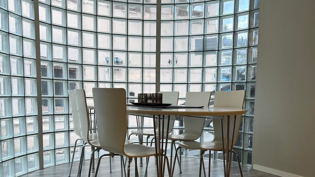 A modern dining area with a large table and chairs, surrounded by large windows with a grid pattern. - Notodden Sentrum Apartment NO 9 (Notodden)