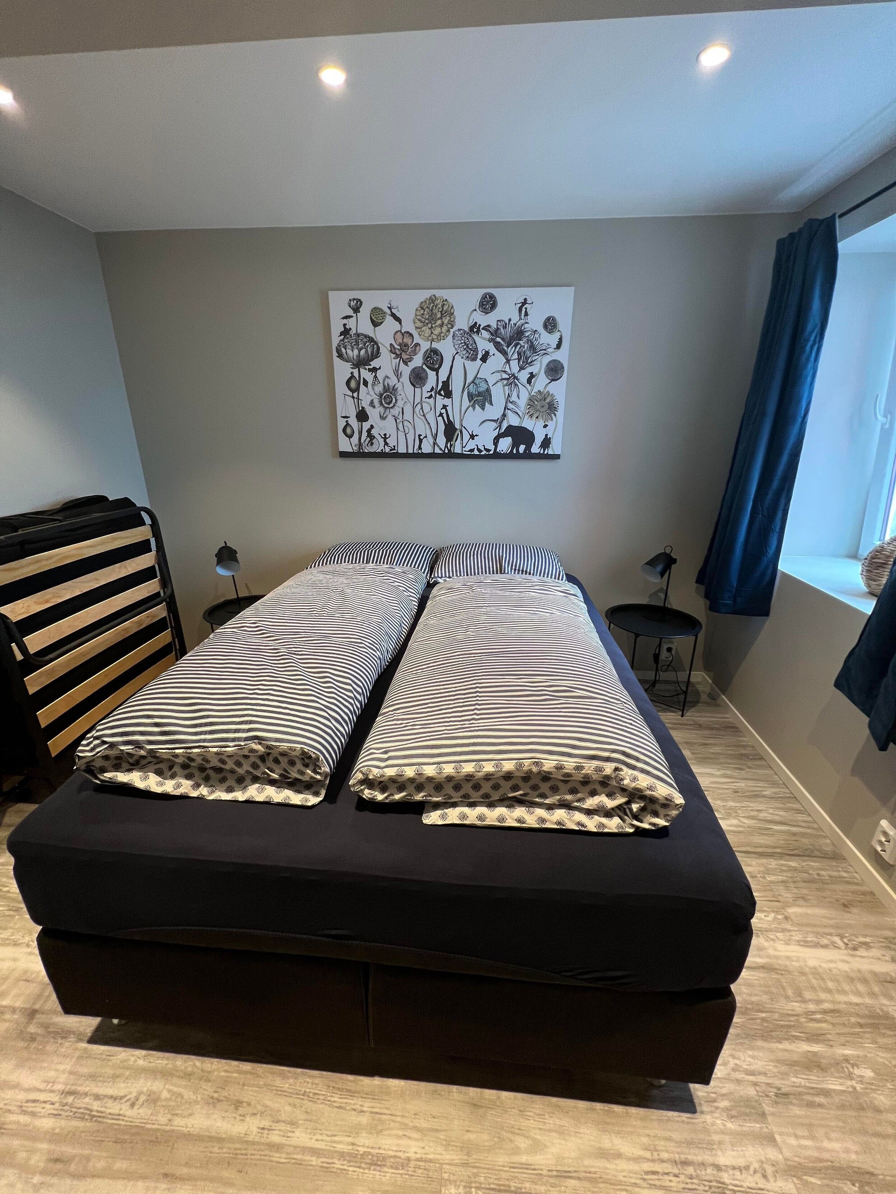 Una camera da letto moderna con un letto grande, una testiera in legno, un'opera d'arte appesa al muro, un tavolino e una finestra con tende.