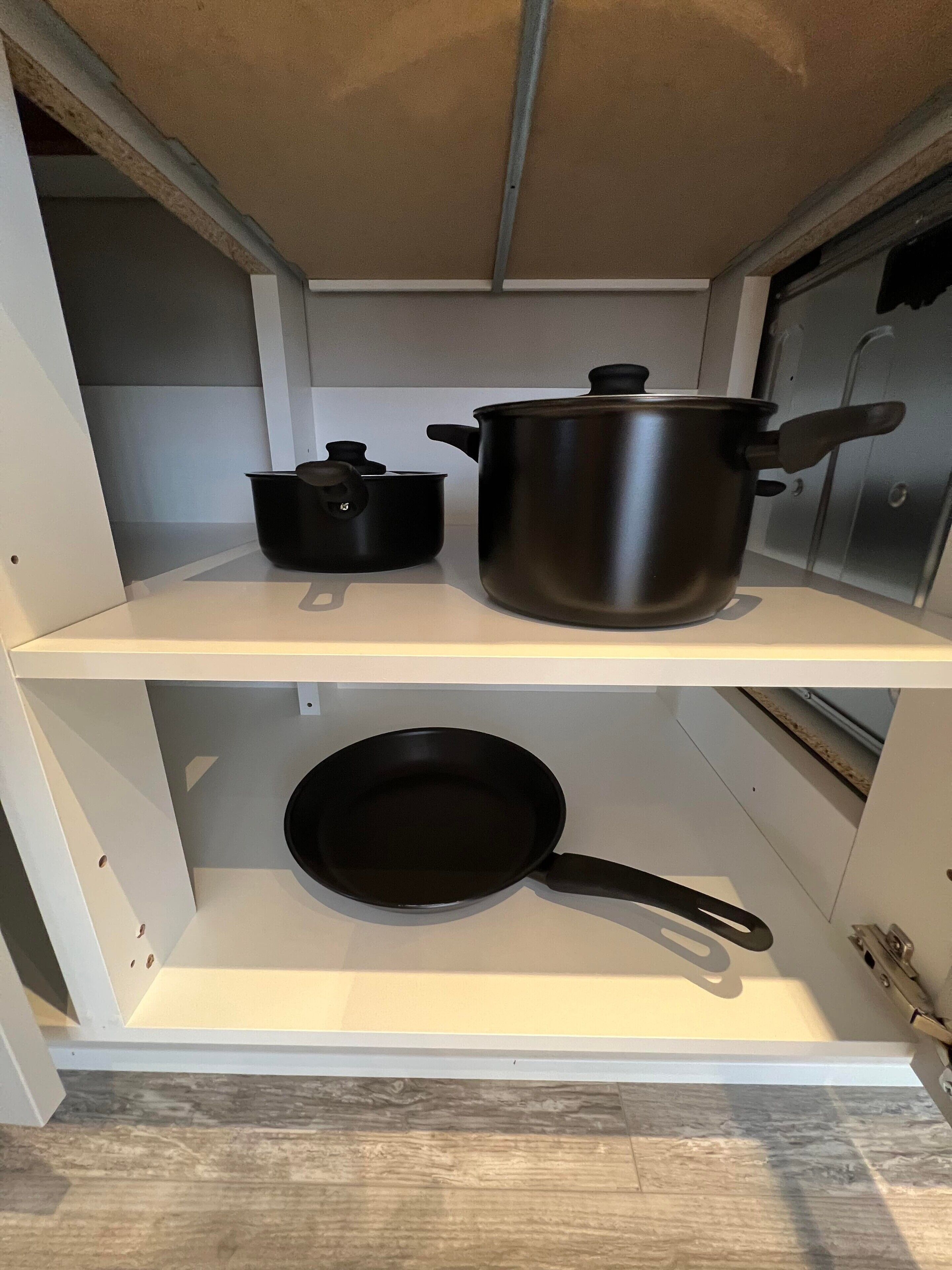 A kitchen shelf with a large pot, a smaller pot, and a frying pan.