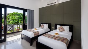Een hotelkamer met twee bedden, een balkon met uitzicht op groen en een airconditioner aan de muur.