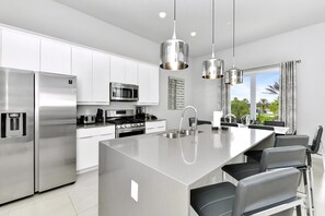 A modern kitchen with stainless steel appliances, a central island, and pendant lighting. - Sleek Two Story Condo near Disney with Resort & Waterpark Access - B27-214 (Kissimmee)