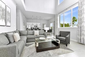 A modern living room with a grey sofa, a glass coffee table, and a dining area with a white table and chairs.