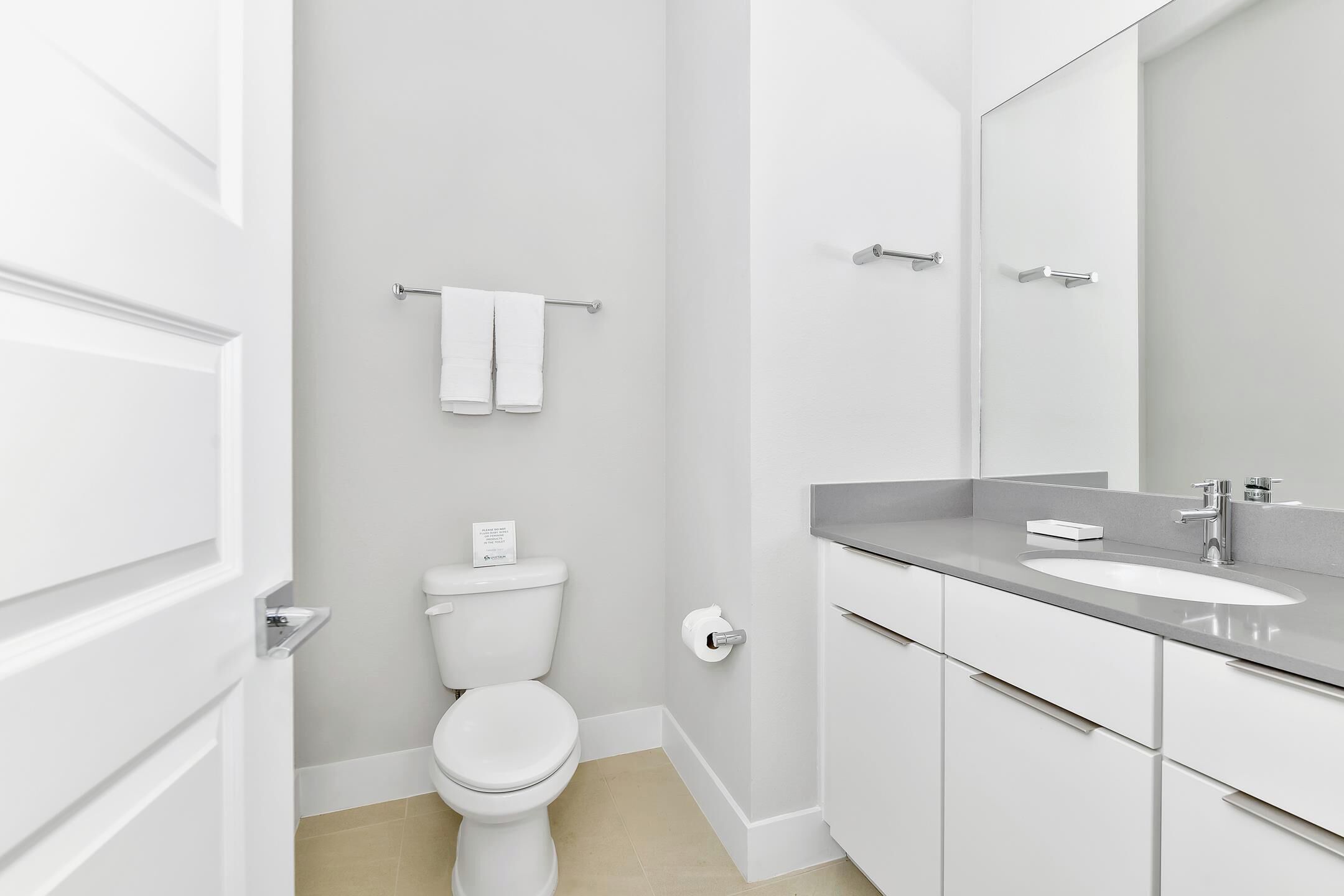 Ein modernes Badezimmer mit Toilette, Handtuchhalter, Waschbecken und Spiegel.
