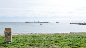 Uma área gramada com um monumento de pedra e um mar calmo com barcos.