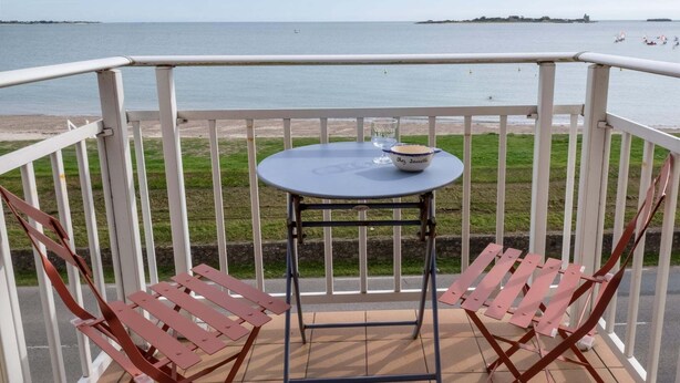 Varanda com mesa e duas cadeiras, vista para a praia e o mar.