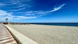 A beach with a clear sky, a concrete walkway, and a few umbrellas.