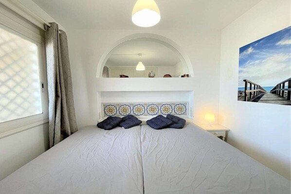 A bedroom with a large bed, a mirror above it, and a painting of a beach on the wall.