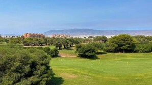 A golf course with a clear view of the surrounding landscape, including distant mountains and a building with multiple floors.