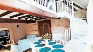 A dining area with a white table and chairs, a blue sofa, and a staircase leading to an upper level. - Geräumiges Ferienhaus mit Garten (BREUGNON)