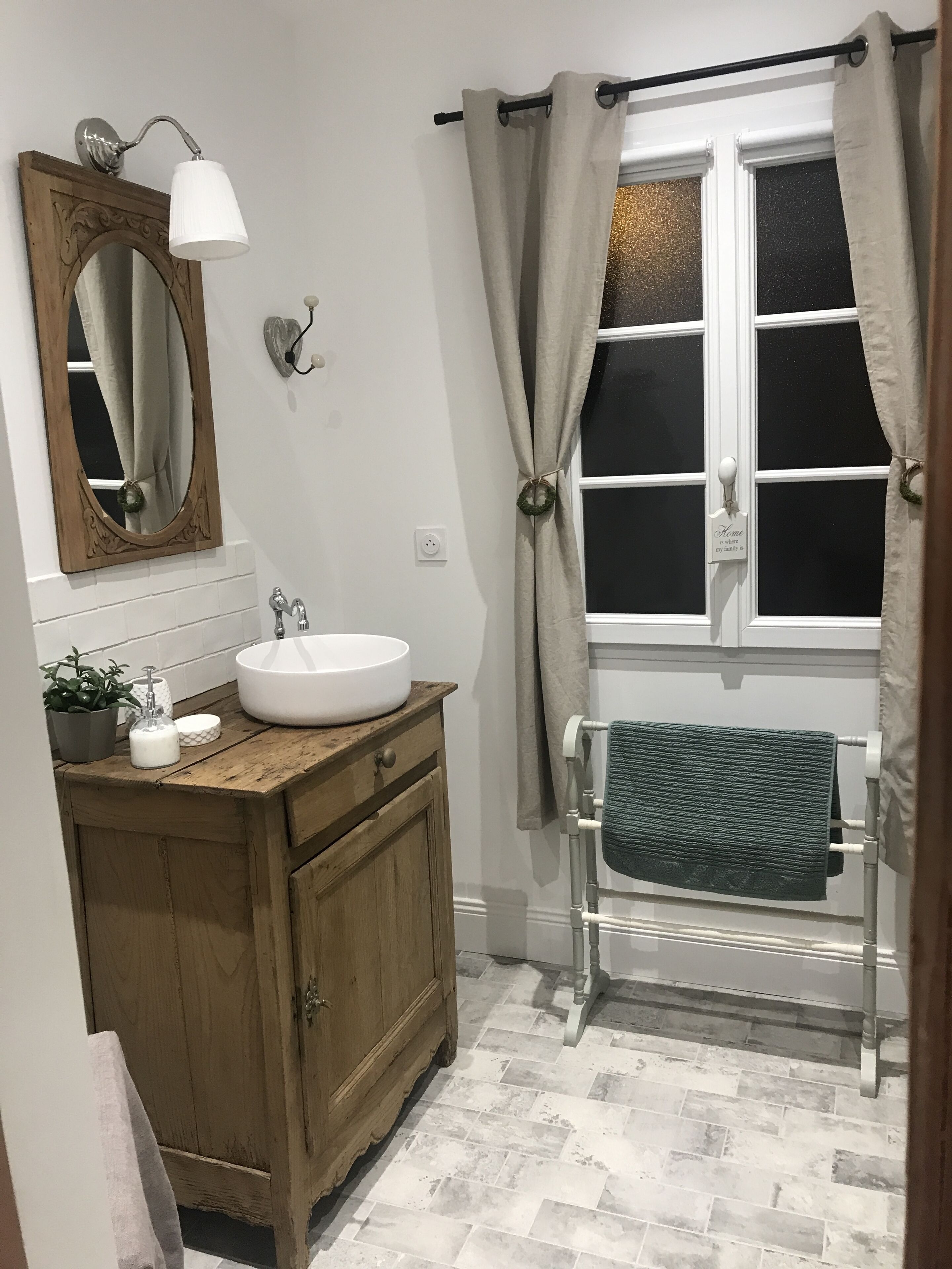 A bathroom with a wooden vanity, a white sink, a mirror, a towel rack, and a window with curtains.