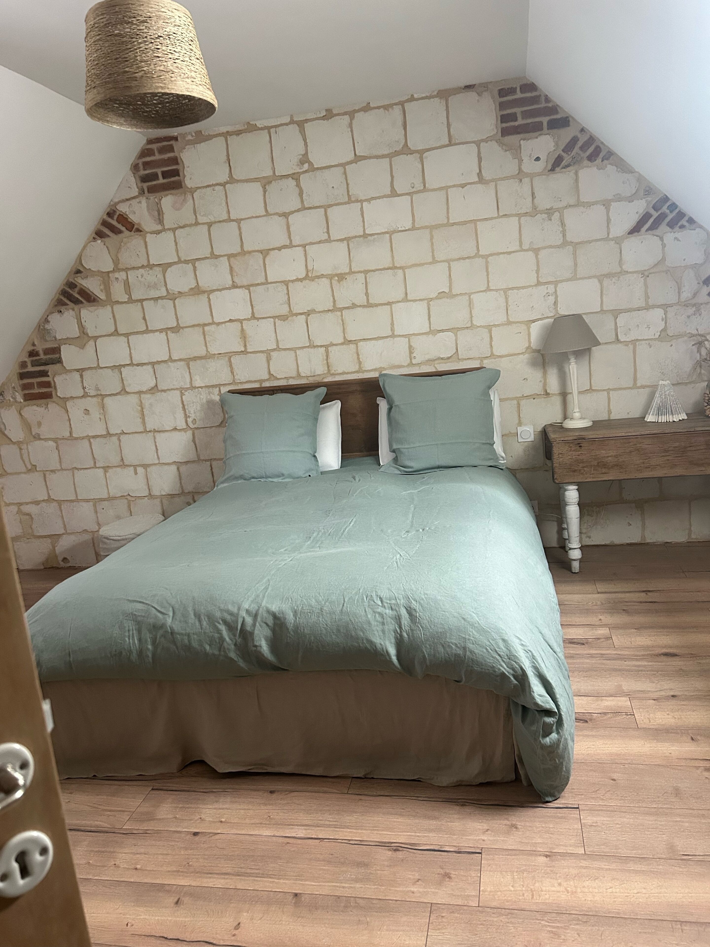 Camera da letto con parete a effetto mattone, pavimento in legno e letto con copriletto e cuscini verdi.