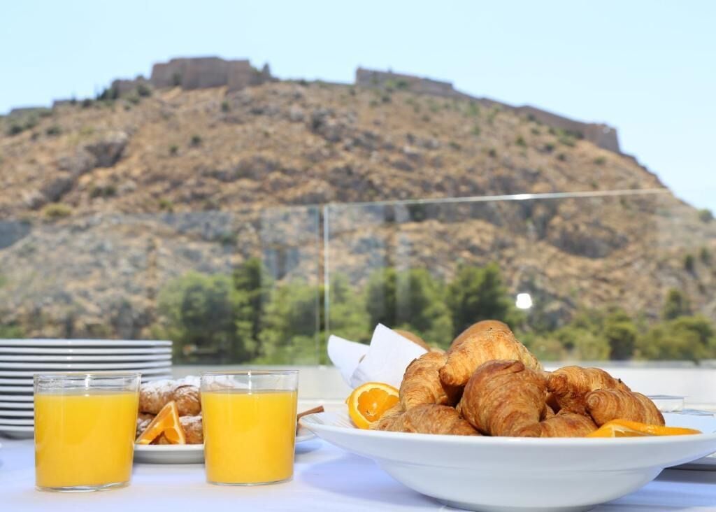 En frukostuppdukning med croissanter, apelsinjuice och en vacker utsikt över en kulle med en fästning.