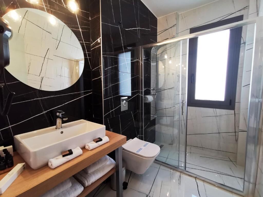 Un baño moderno con un espejo ovalado grande, un lavabo rectangular, una cabina de ducha con paredes de cristal y un inodoro.