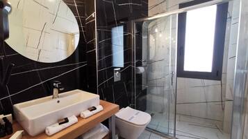 Un baño moderno con un espejo ovalado grande, un lavabo rectangular, una cabina de ducha con paredes de cristal y un inodoro.