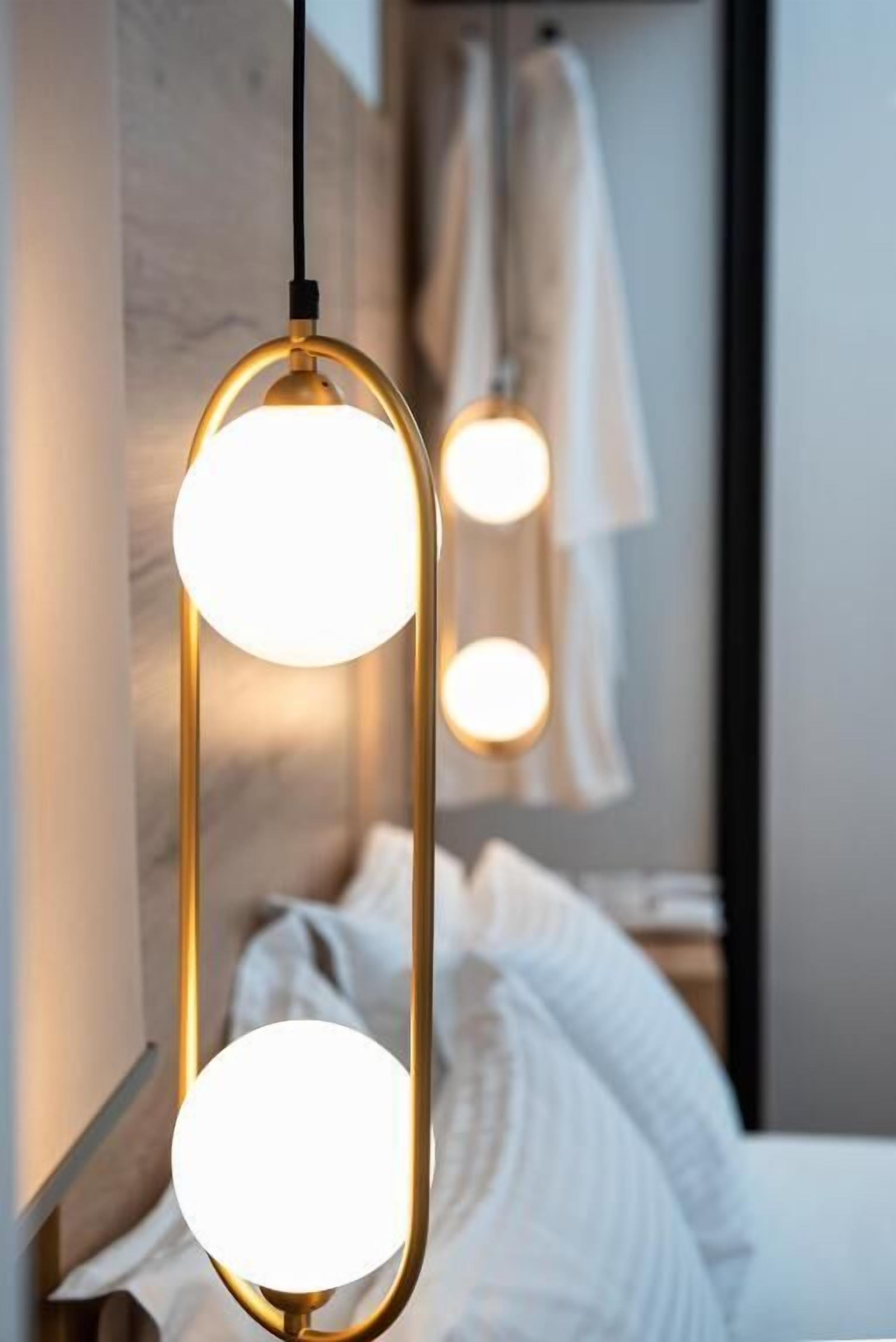 Une chambre d’hôtel moderne avec un lit, une tête de lit en bois et un luminaire suspendu.