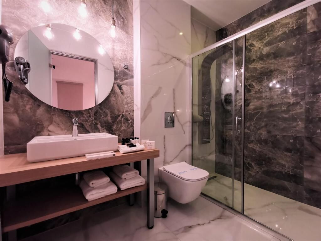 Een moderne badkamer met een marmeren wastafelmeubel, een ronde spiegel, een glazen douchecabine en een toilet.