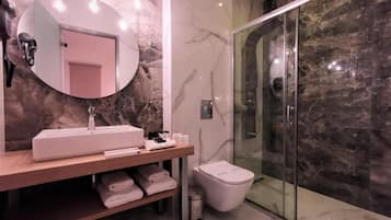 Een moderne badkamer met een marmeren wastafelmeubel, een ronde spiegel, een glazen douchecabine en een toilet.