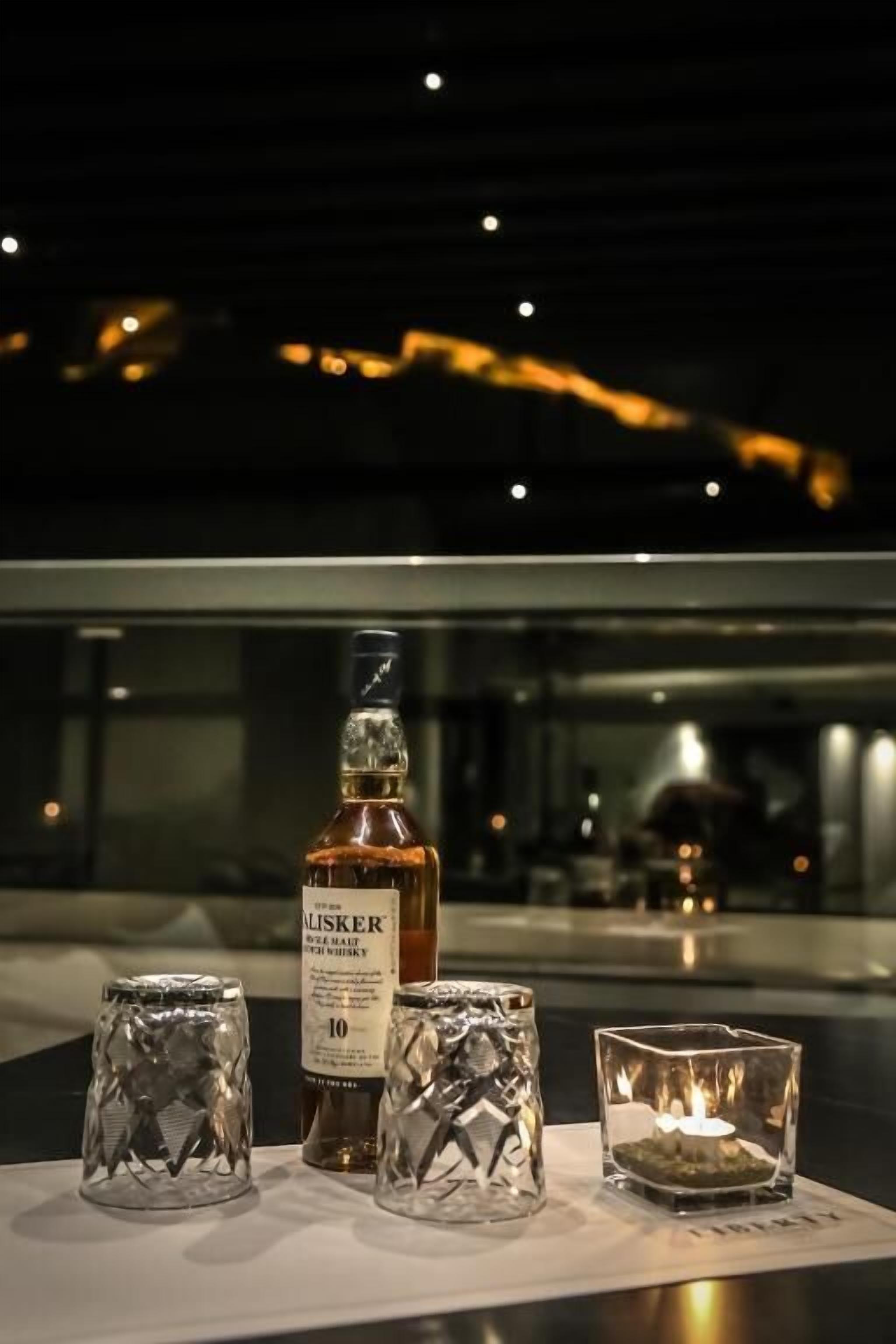 Uma garrafa de uísque e três decanters de vidro sobre uma mesa com uma vela.