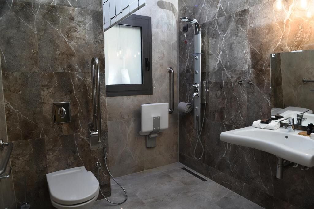 Ein modernes Badezimmer mit Toilette, einer Dusche inklusive Handbrause, einem Waschbecken mit Spiegel und einem Fenster über der Toilette.