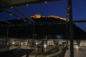 Un espacio exterior para comer con mesas y sillas, con vistas a un paisaje montañoso al atardecer.