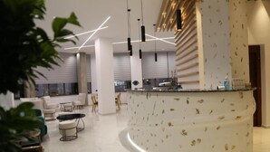 A modern lobby with a curved reception desk, seating area with sofas and chairs, and pendant lighting. - Liberty Hotel of Nafplio (Nafplio)